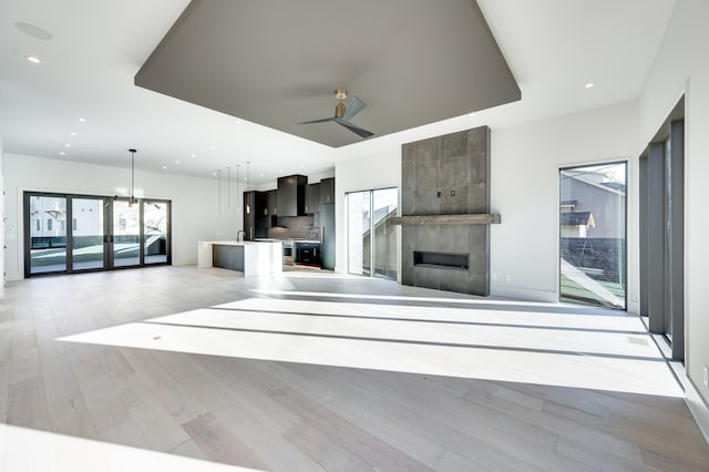 unfurnished living room with light hardwood / wood-style floors, a tile fireplace, and ceiling fan