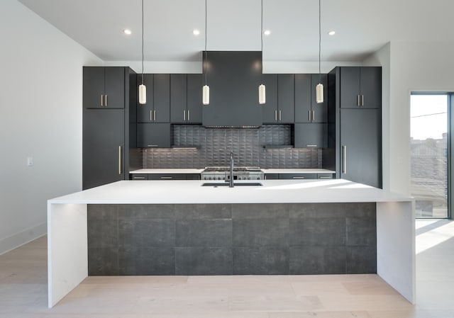 kitchen featuring sink, a kitchen island with sink, decorative light fixtures, and extractor fan