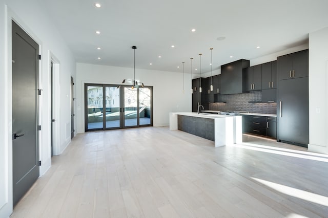 kitchen with an island with sink, light hardwood / wood-style flooring, decorative light fixtures, and tasteful backsplash