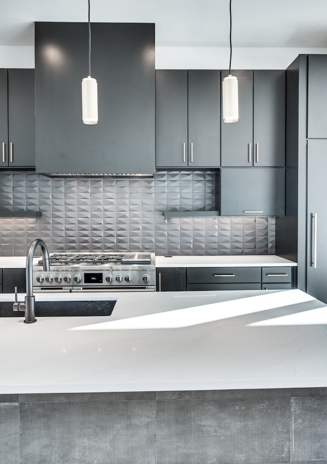 kitchen with backsplash, pendant lighting, stainless steel range, and light stone counters