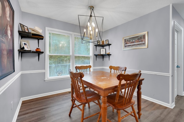 dining area with dark wood-type flooring, a textured ceiling, and an inviting chandelier