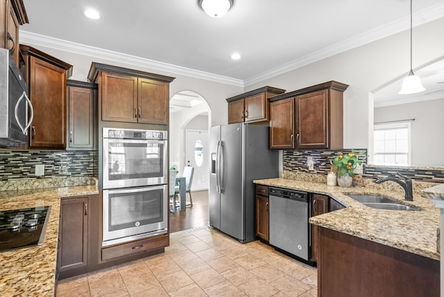 kitchen featuring hanging light fixtures, stainless steel appliances, sink, crown molding, and light stone counters