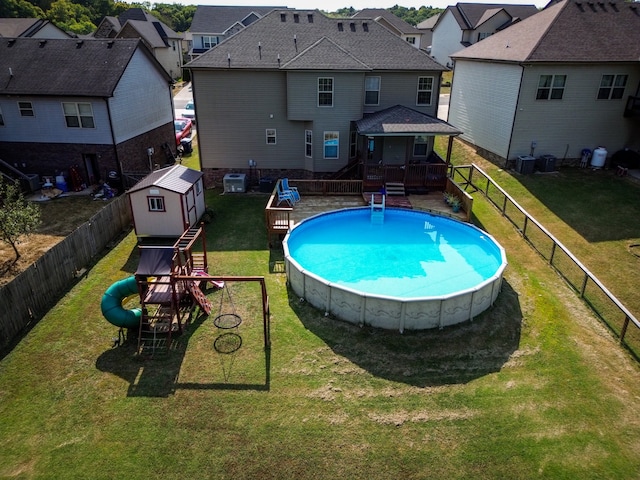 view of pool with central air condition unit, a storage shed, a lawn, and a wooden deck