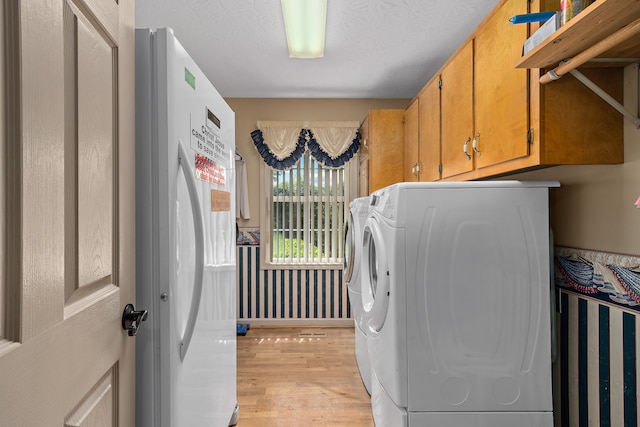 clothes washing area with separate washer and dryer, a textured ceiling, light hardwood / wood-style floors, and cabinets