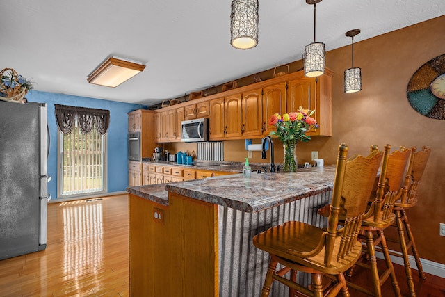 kitchen with kitchen peninsula, a breakfast bar area, stainless steel appliances, light hardwood / wood-style floors, and decorative light fixtures