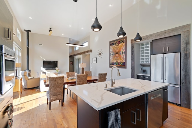 kitchen with a high ceiling, a center island with sink, sink, appliances with stainless steel finishes, and dark brown cabinets