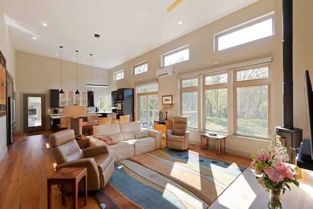 living room with hardwood / wood-style flooring, a wall unit AC, a wood stove, and a high ceiling