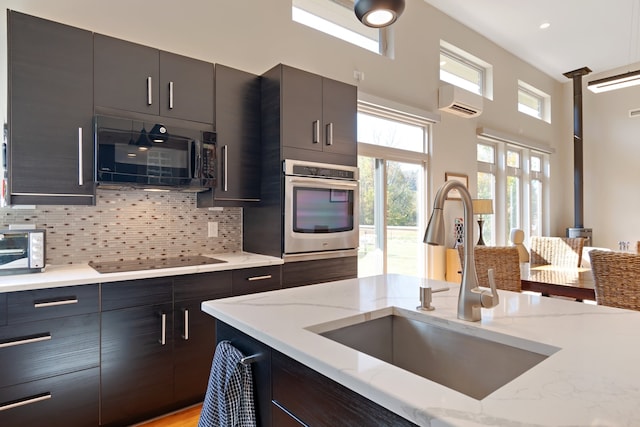 kitchen with sink, tasteful backsplash, light stone counters, a wall mounted AC, and black appliances