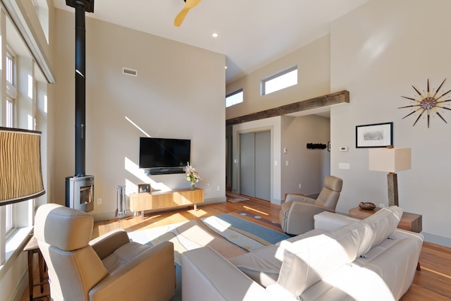 living room featuring a wood stove, light hardwood / wood-style flooring, and a towering ceiling