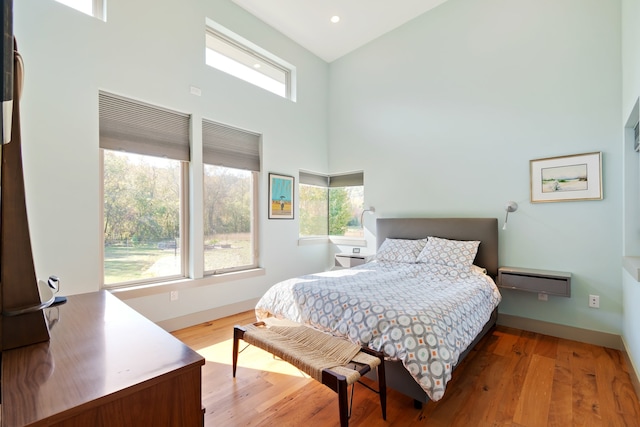 bedroom featuring a towering ceiling and light hardwood / wood-style flooring