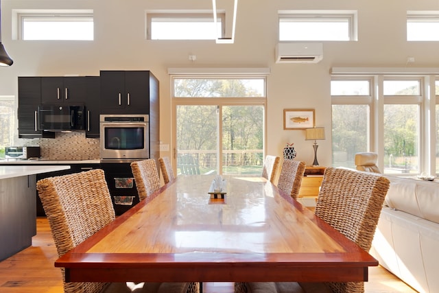 dining space with a wall mounted AC, a towering ceiling, light wood-type flooring, and plenty of natural light