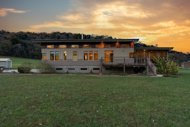 back house at dusk featuring a deck and a lawn