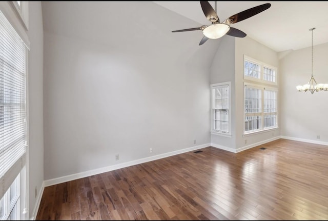 empty room with high vaulted ceiling, ceiling fan with notable chandelier, and hardwood / wood-style flooring