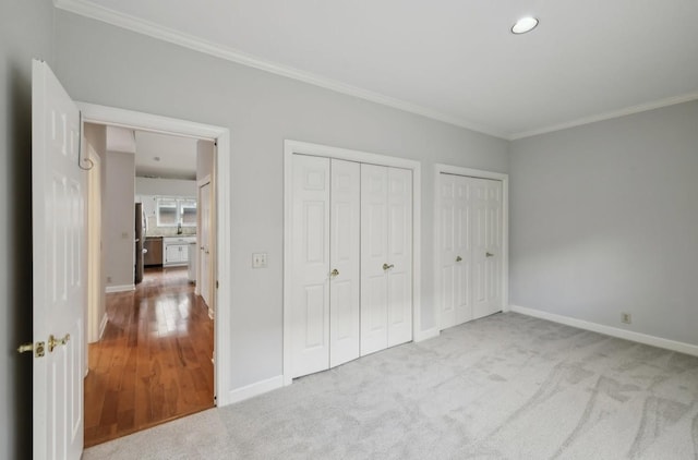 unfurnished bedroom with light carpet, stainless steel fridge, two closets, and crown molding