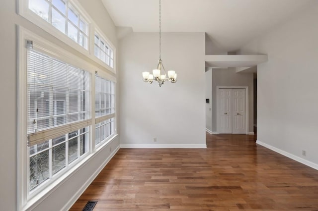 unfurnished dining area with a notable chandelier, wood-type flooring, and a towering ceiling