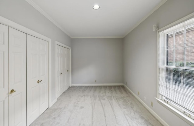 unfurnished bedroom with light colored carpet, ornamental molding, and two closets