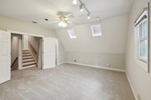 basement with ceiling fan, a healthy amount of sunlight, light colored carpet, and rail lighting