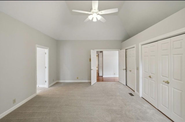 unfurnished bedroom featuring ceiling fan, light colored carpet, lofted ceiling, and multiple closets