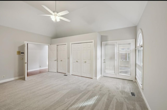 unfurnished bedroom featuring light colored carpet, vaulted ceiling, ceiling fan, and multiple closets