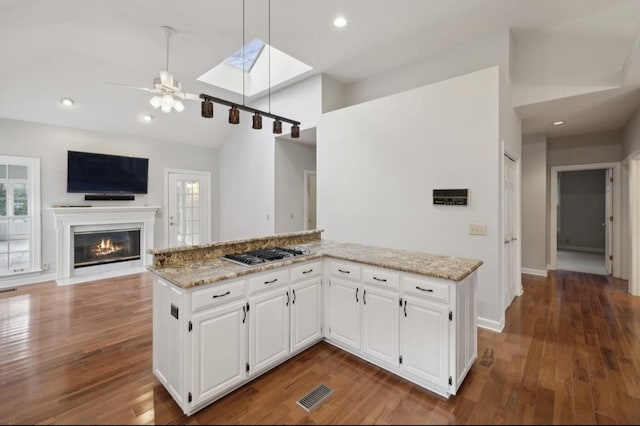 kitchen featuring white cabinetry, light stone countertops, hanging light fixtures, stainless steel gas cooktop, and hardwood / wood-style floors