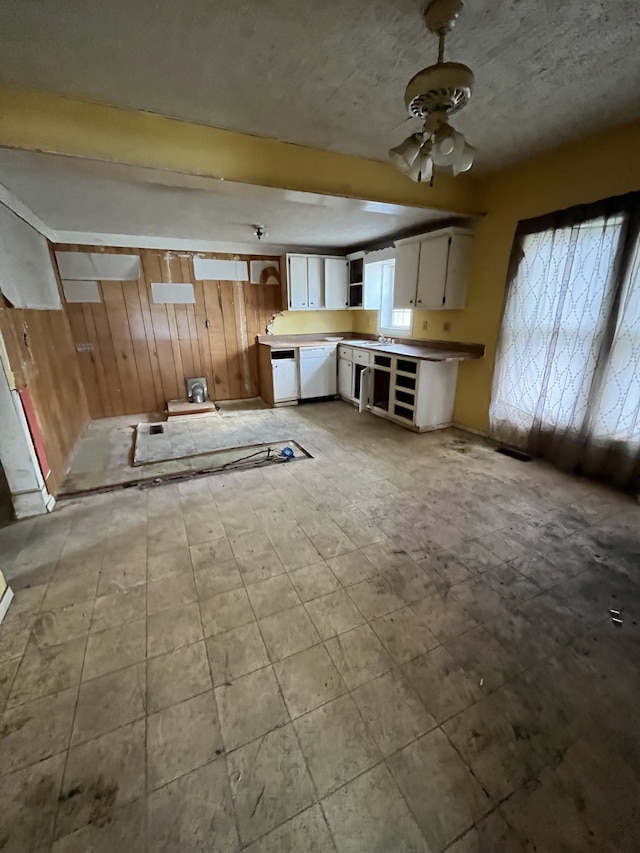 kitchen with white cabinetry, ceiling fan, white dishwasher, and wooden walls