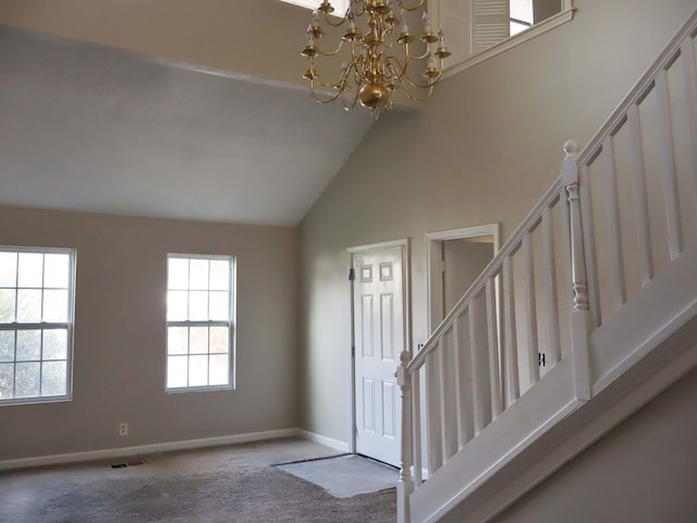 carpeted foyer entrance with high vaulted ceiling and an inviting chandelier