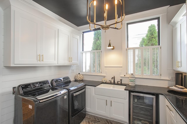 washroom with beverage cooler, washing machine and dryer, cabinets, an inviting chandelier, and sink