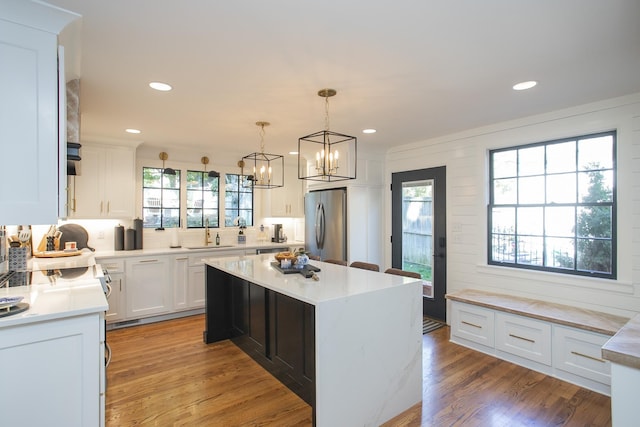 kitchen with decorative light fixtures, a kitchen island, light wood-type flooring, stainless steel appliances, and white cabinets