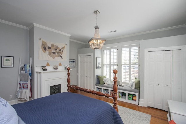 bedroom with an inviting chandelier, light wood-type flooring, ornamental molding, and multiple closets