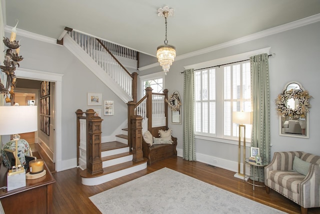 foyer entrance with dark wood-type flooring, ornamental molding, and a notable chandelier