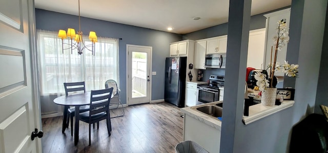 kitchen with hardwood / wood-style floors, an inviting chandelier, white cabinets, hanging light fixtures, and appliances with stainless steel finishes