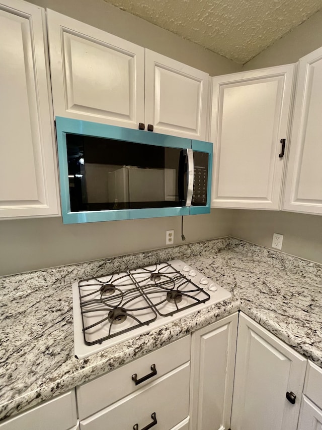 kitchen with a textured ceiling, white cabinets, and white gas cooktop