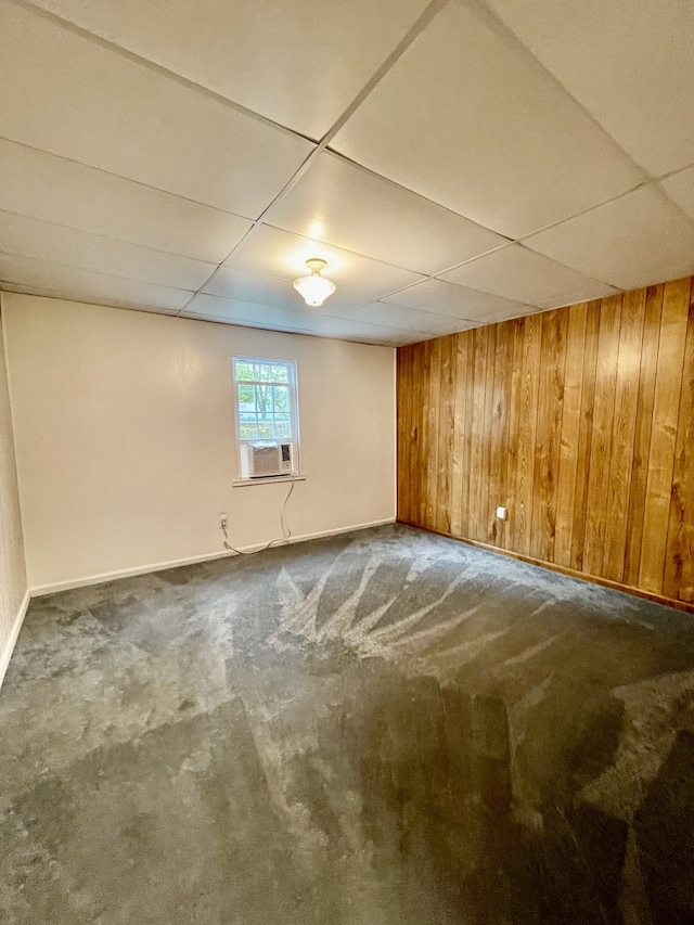 basement featuring dark carpet, wooden walls, and a paneled ceiling