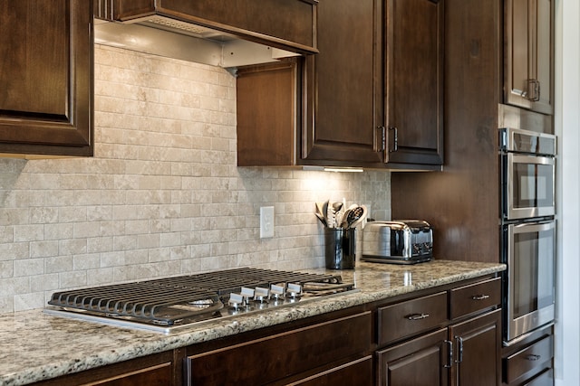 kitchen featuring decorative backsplash, dark brown cabinets, stainless steel appliances, and light stone countertops