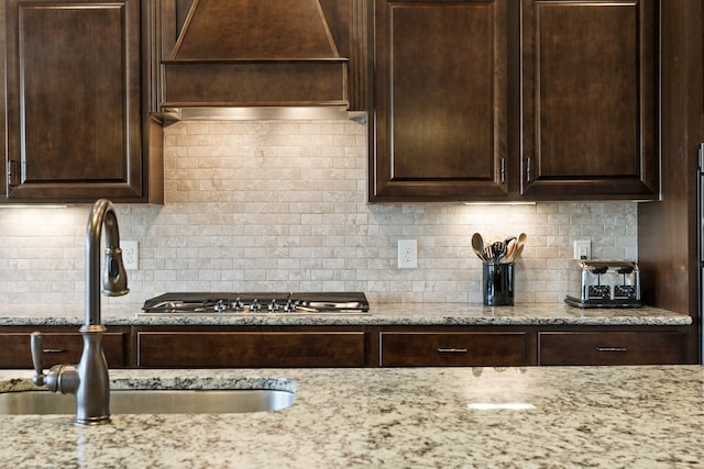 kitchen with decorative backsplash, dark brown cabinetry, light stone countertops, and sink