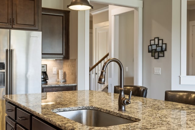 kitchen with high end refrigerator, dark brown cabinetry, light stone counters, and sink