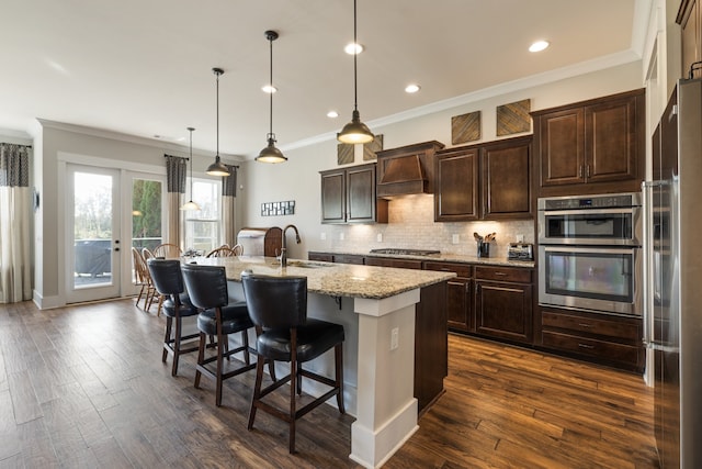 kitchen featuring dark hardwood / wood-style flooring, pendant lighting, a center island with sink, appliances with stainless steel finishes, and ornamental molding