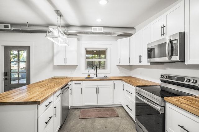 kitchen with appliances with stainless steel finishes, sink, wood counters, white cabinetry, and pendant lighting