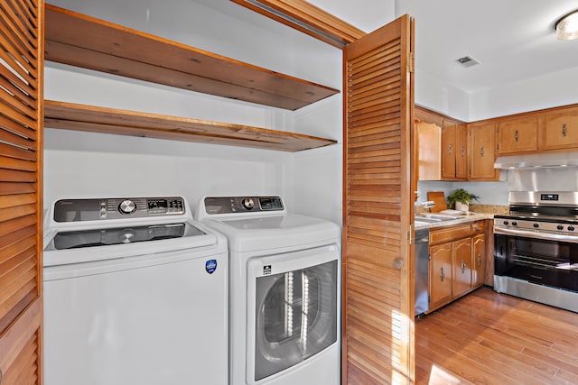 washroom with washing machine and dryer, sink, and light wood-type flooring