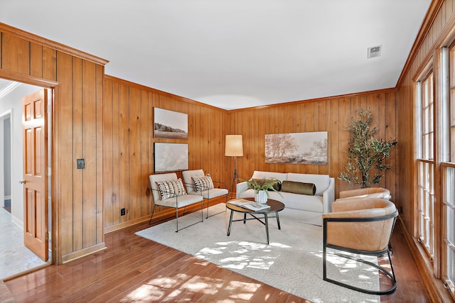 living room with ornamental molding, wooden walls, and wood-type flooring