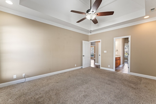 unfurnished bedroom with ceiling fan, a tray ceiling, connected bathroom, crown molding, and light colored carpet