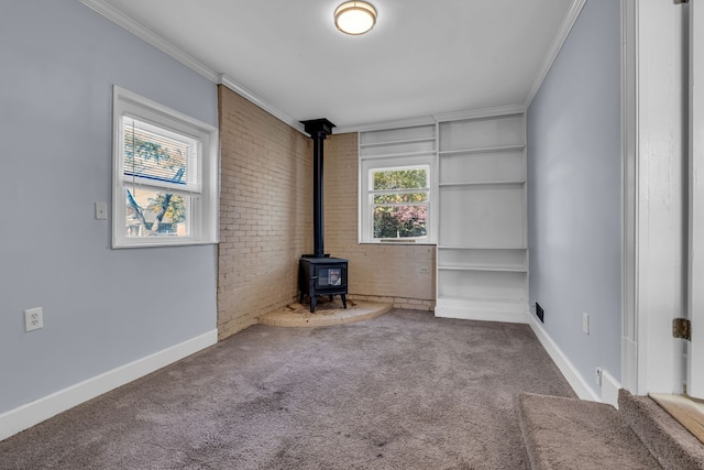 unfurnished living room featuring a wood stove, ornamental molding, brick wall, and carpet floors