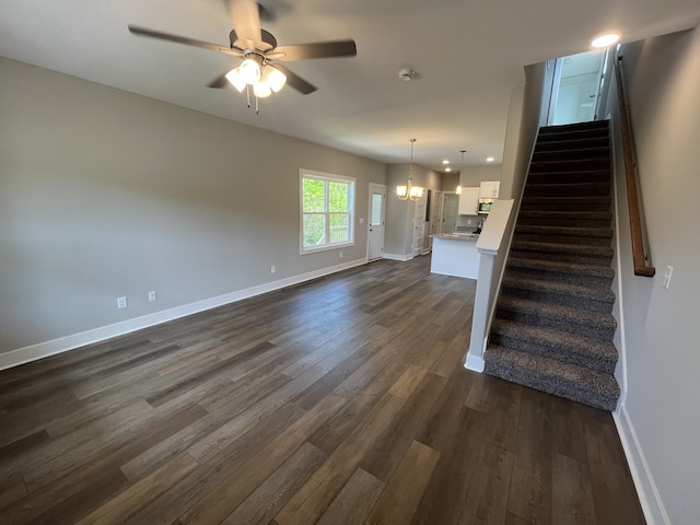 unfurnished living room featuring dark wood-type flooring and ceiling fan with notable chandelier