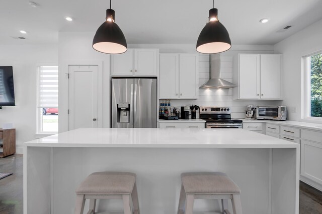 kitchen with stainless steel appliances, wall chimney range hood, decorative light fixtures, and a kitchen island