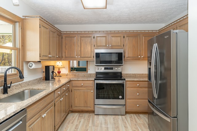 kitchen with sink, light stone countertops, light wood-type flooring, appliances with stainless steel finishes, and a textured ceiling