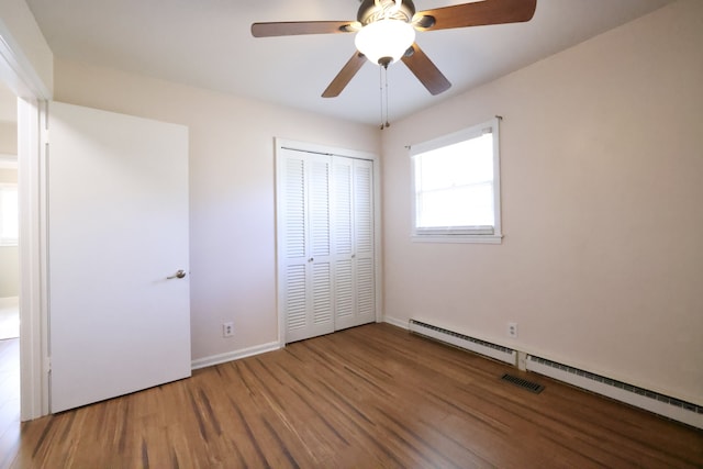 unfurnished bedroom featuring a closet, ceiling fan, wood-type flooring, and a baseboard heating unit