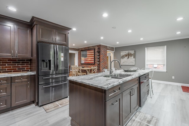 kitchen featuring sink, light wood-type flooring, an island with sink, stainless steel appliances, and ornamental molding