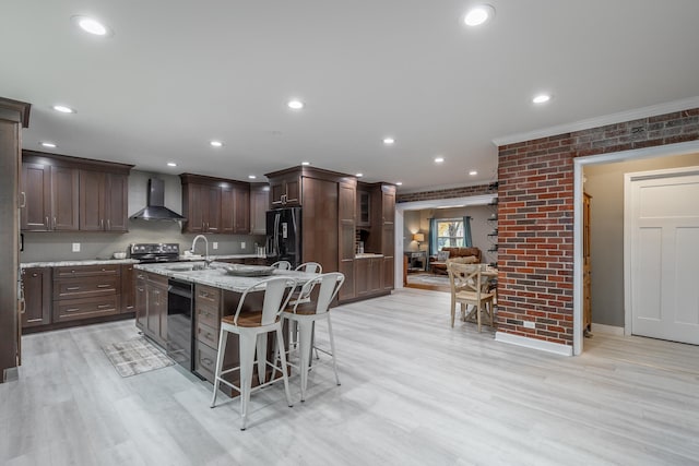 kitchen with wall chimney range hood, sink, black refrigerator with ice dispenser, light hardwood / wood-style floors, and a kitchen island with sink