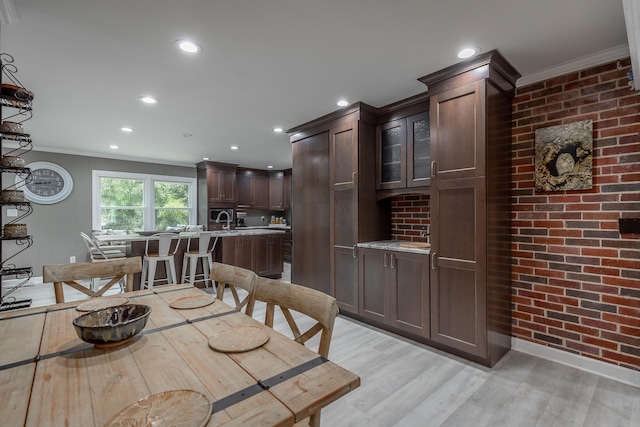 dining space featuring light hardwood / wood-style floors, crown molding, and brick wall