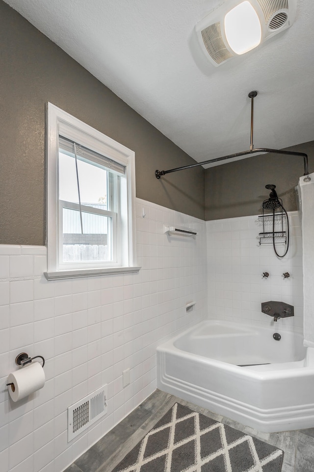 bathroom with hardwood / wood-style floors, tiled shower / bath combo, and tile walls